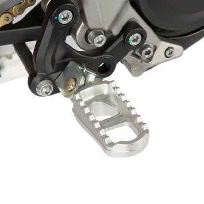 Close-up of a motorcycle foot peg with chain and sprocket in the background