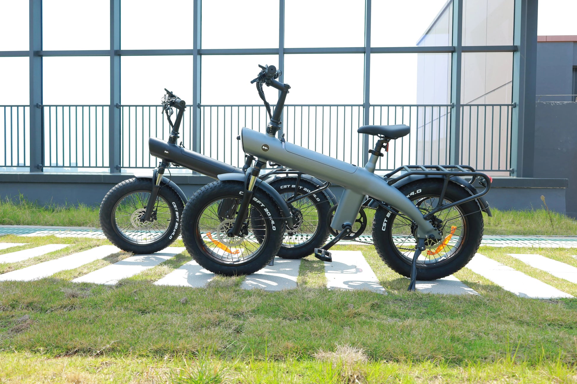 Three electric bicycles parked on a grassy area with a building in the background
