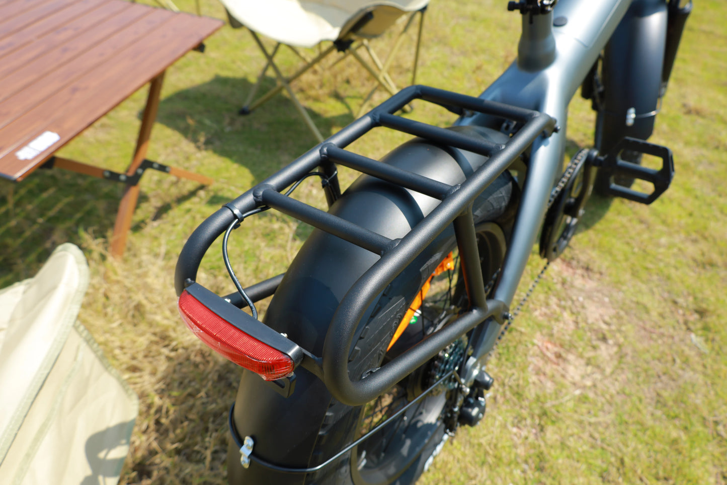 Bicycle with a rear rack and red reflector on a grassy area with a wooden table and chair in the background.