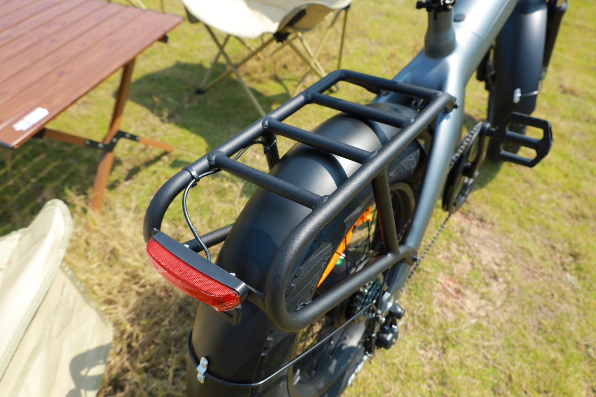 Bicycle with a rear rack and red reflector on a grassy area with a wooden table and chair in the background.