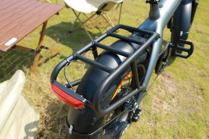 Bicycle with a rear rack and red reflector on a grassy area with a wooden table and chair in the background.