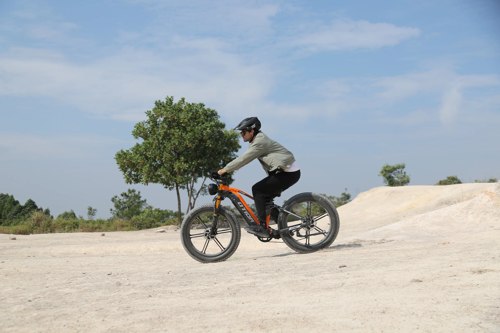 Person riding a bicycle on a sandy terrain with trees in the background