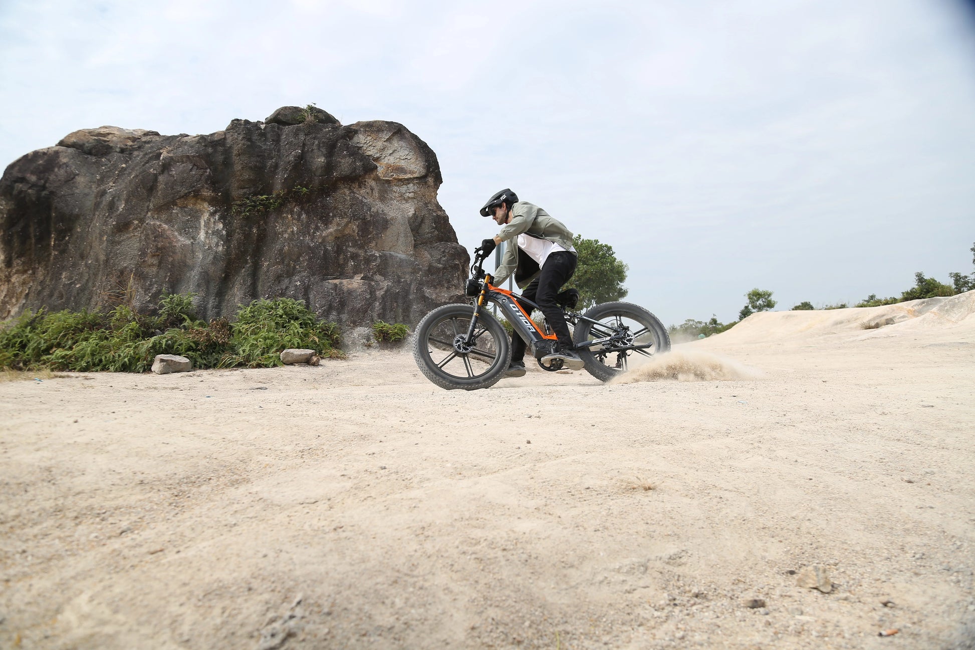 Person riding a mountain bike on a dirt trail with rocky outcrops in the background