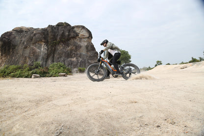 Person riding a mountain bike on a dirt trail with rocky outcrops in the background
