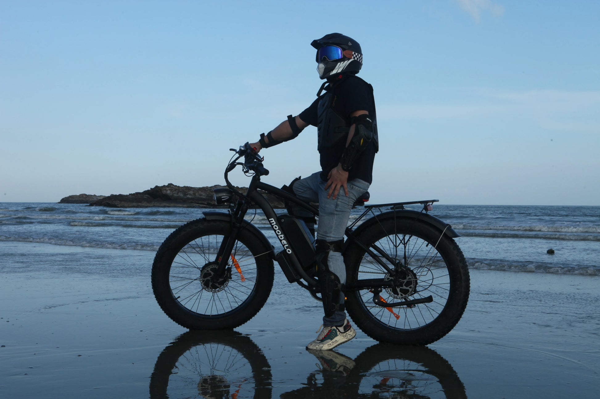 Person on a beach with a bike, wearing a helmet and black jacket.