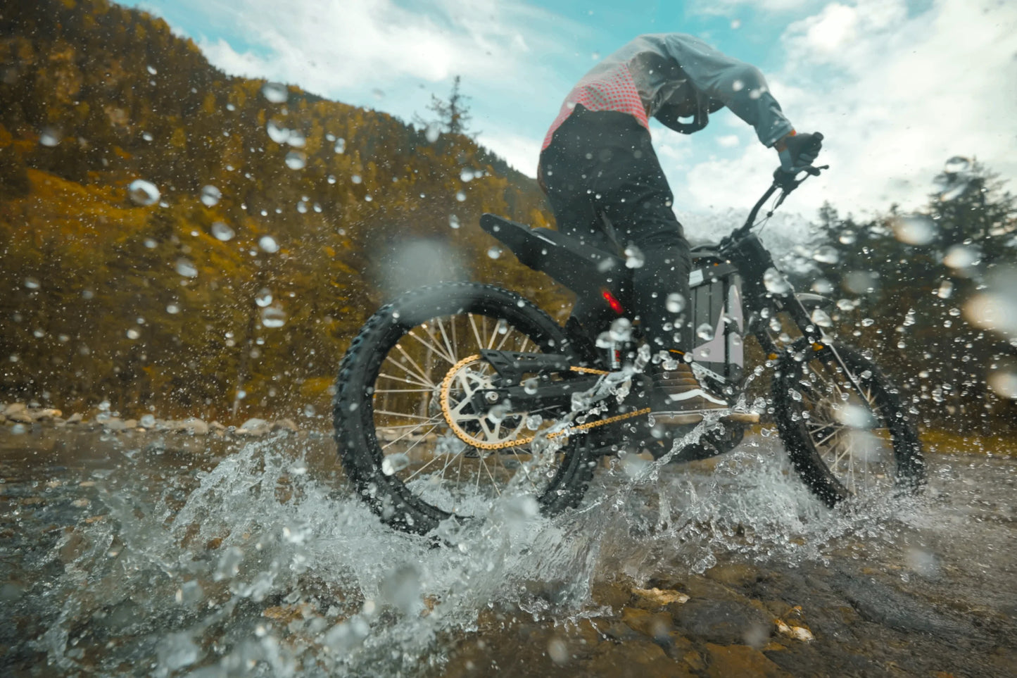 Person riding a motorcycle through water with a mountainous background