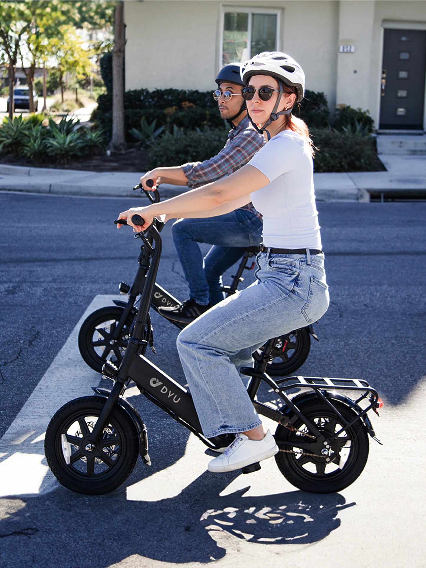 Two people riding electric bikes on a street with a house in the background